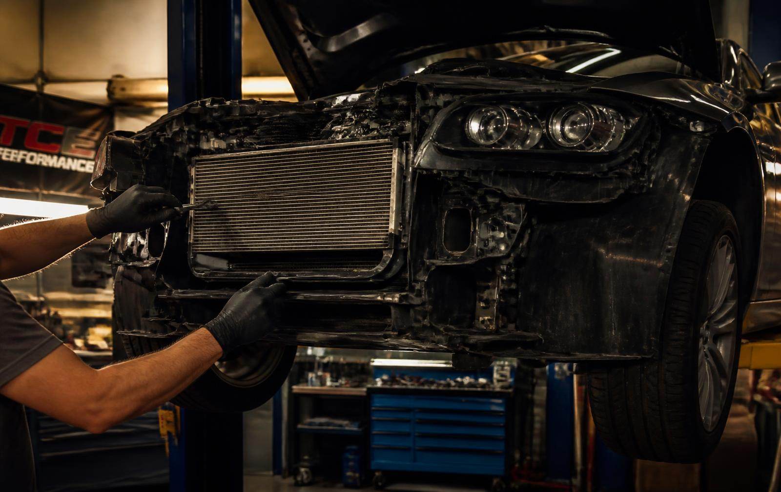 Mechanic removing a radiator from the front of a car raised on a lift inside the shop